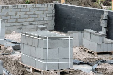 Temel duvarının içinde siyah asfalt bazlı bir karışım içeren nemli bir yalıtım, paletlerin üzerinde beton bloklar ve plastik bir kova olan bir inşaat alanı.