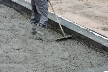 Tırmıkla beton döşeyen bir inşaatçı.