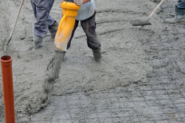 Beton bir kamyonun hortumunu kullanarak beton bir temel döken bir inşaat işçisi ve bir tırmıkla betonu düzleştirip yayan bir müteahhit.