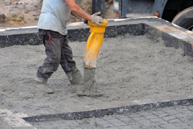Beton bir kamyonun hortumunu kullanarak beton bir temel döken bir inşaat işçisi.