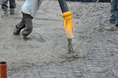 A building worker pouring a concrete slab foundation using a hose of a concrete pump truck and a builder levelling and spreading concrete with a rake clipart