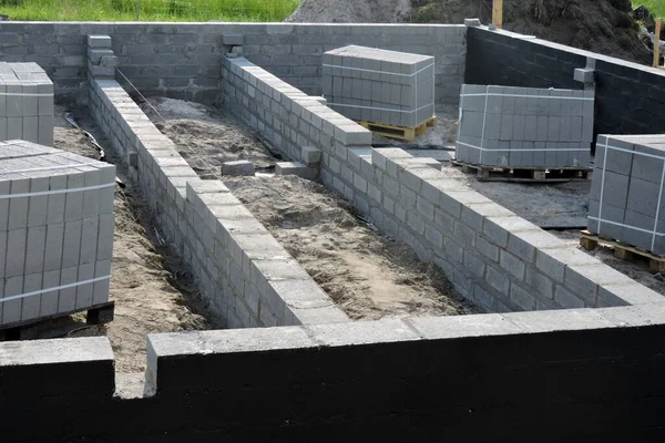 Dış fondöten duvarını siyah asfalt bazlı karışımla nemlendiriyor. Paletlerin üzerinde beton bloklar olan bir inşaat alanı.