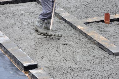 Tırmıkla beton döşeyen bir inşaatçı.