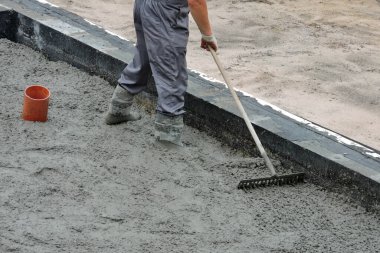 Tırmıkla beton döşeyen bir inşaatçı.
