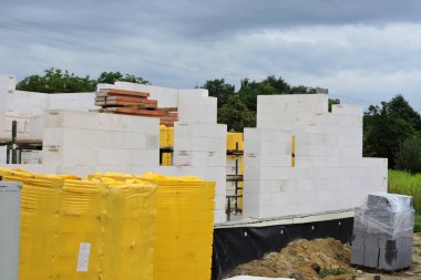 İnşaat halindeki bir ev, acc bloklardan yapılmış duvarlar, kaba pencereler ve kapı açıkları, güçlendirilmiş tuğla kiremitler, yalıtımlı temel duvarlar, paletlere beton bloklar ve akc bloklar.