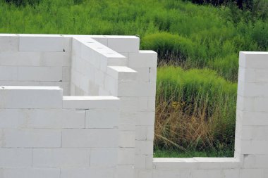 İnşaat halinde bir ev, otomatik klavsenli beton bloklardan yapılmış duvarlar, arka planda sert bir pencere açılması, bazı ağaçlar.