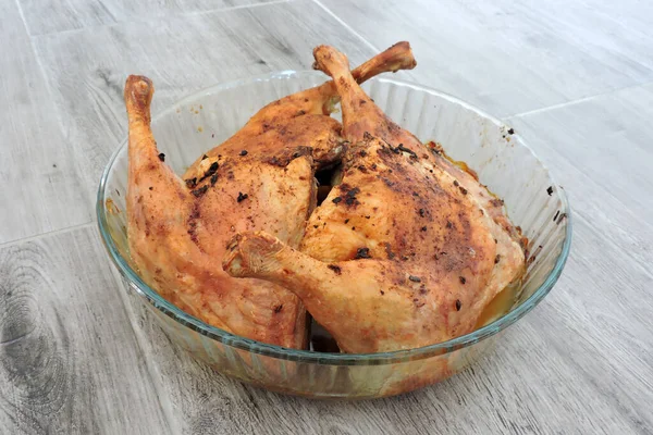 Four seasoned roasted whole chicken legs in a glass heat-resistant vessel, the grey wooden background