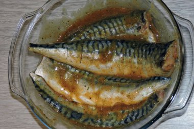 Camda terbiye edilmiş dört taze uskumru, ısıya dayanıklı kap, gri ahşap arka plan.