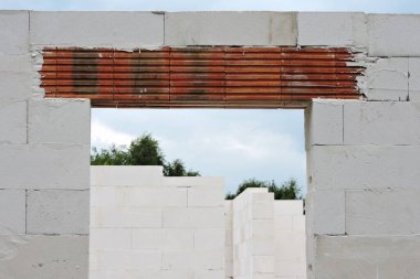 Güçlendirilmiş tuğla kaplama, kaba bir kapı açılışı ve arka planda otoklava betondan, yeşil ağaçlardan ve mavi gökyüzünden yapılmış duvarlar.