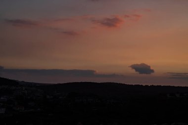 Gün batımında kısmen bulutlu gökyüzü, İsrail 'in Celile dağlarındaki bir köyün üzerinde kırmızıya döner..