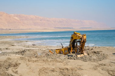Sisli bir sabahta, ölü deniz kıyısında çamura saplanmış ağır bir kazıcı..