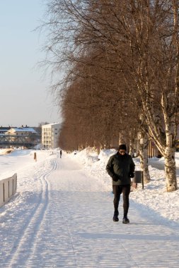 Rovaniemi, Finlandiya - 17 Mart 2022: Donmuş Kemijoki nehrinin kıyısında karlı bir yolda koşan bir adam, Rovaniemi, Finlandiya.