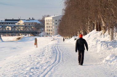 Rovaniemi, Finlandiya - 17 Mart 2022: Donmuş Kemijoki nehrinin kıyısında karlı bir yolda yürüyen bir kişi, Rovaniemi, Finlandiya.