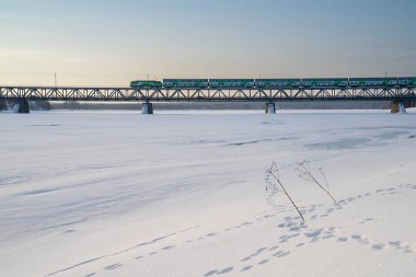 Rovaniemi, Finlandiya - 17 Mart 2022: Şafak vakti donmuş Kemijoki nehri üzerindeki köprüden geçen bir tren..