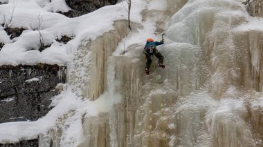 Finlandiya 'da donmuş bir şelalenin buz duvarına tırmanan bir uçurum tırmanıcısı.