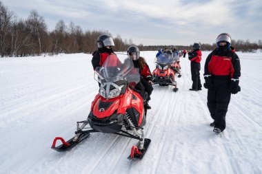 Rovaniemi, Finlandiya - 20 Mart 2022: Finlandiya 'da donmuş bir nehirde kar aracı turuna hazırlanan bir grup turist.