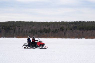 Rovaniemi, Finlandiya - 20 Mart 2022: Finlandiya 'da donmuş bir nehirde kar aracına binen iki turist.