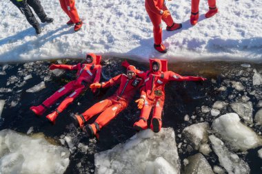 Rovaniemi, Finlandiya - 21 Mart 2022: Eriyen baltık denizinin donmuş sularında yalıtkan giysiler kullanarak yüzen bir grup turist.