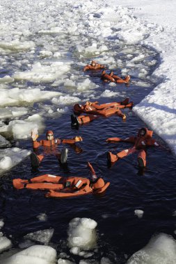 Rovaniemi, Finlandiya - 21 Mart 2022: Eriyen baltık denizinin donmuş sularında yalıtkan giysiler kullanarak yüzen bir grup turist.