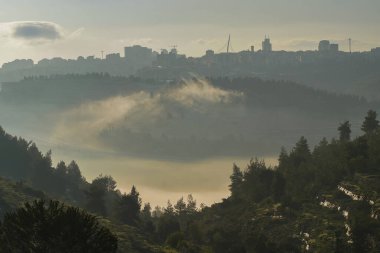 Kudüs 'ün kuzeyindeki bir vadide sisli bir sabahta bir bulut sürünüyor. Arka planda Kudüs silueti var..