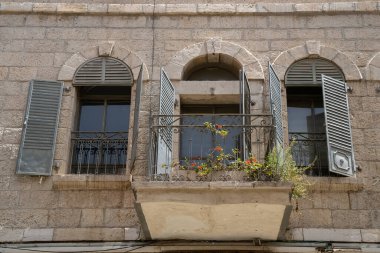 Jerusalem, Israel - April 30th, 2022: A typical balcony, with arched windows and metal window blinds, in a stone house in old Jerusalem, Israel.