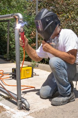 Jerusalem, Israel - May 18th, 2022: A man welding a metal railing outdoors on a sunny day.