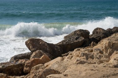İsrail 'in Tel Aviv kentindeki kayalık bir sahilde açık ve güneşli bir günde bir dalga kopuyor..