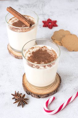 İki bardak yumurtalı kokteyl ve gri arka planda Noel süslemeleri.