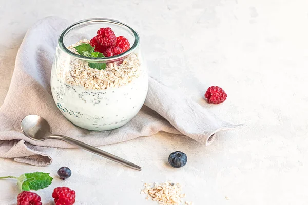 Un vaso con yogur en capas, semillas de chía, avena y bayas, servido para el desayuno —  Fotos de Stock