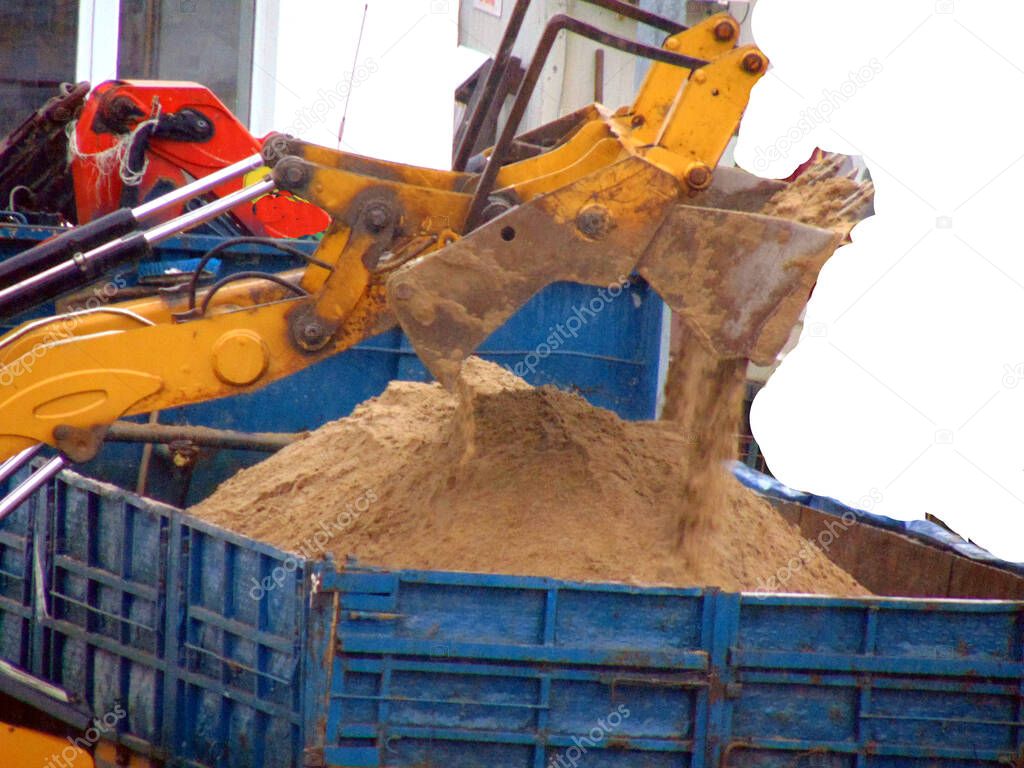 an excavator unloads sand from the bucket into a dump truck