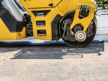 Bir sıkıştırıcı yola taze asfalt döker.