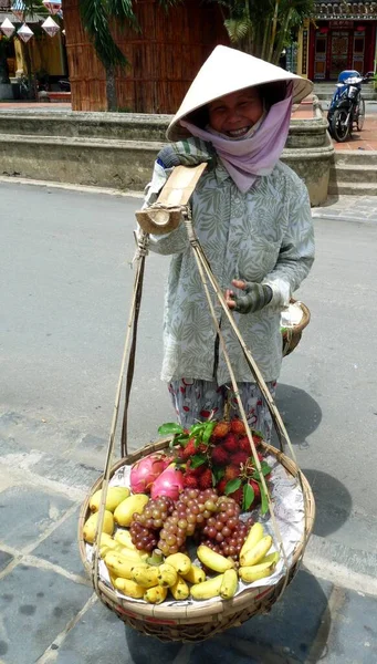 Detailní záběr usmívajícího se prodavače ovoce v kuželovitém klobouku, Hoi An street, Vietnam Stock Obrázky