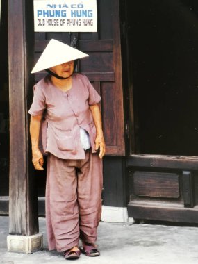 Koni şapkalı yaşlı kadın kapının önünde duruyor, Hoi An, Vietnam.
