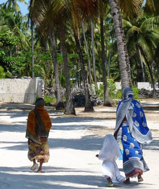 Two local women and child walking by palm trees, Jambiani, Zanzibar