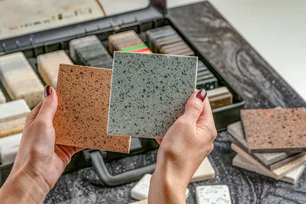 Samples of material for the countertop. Female hands are choosing interior elements for renovation. Samples of acrylic stone in hands.