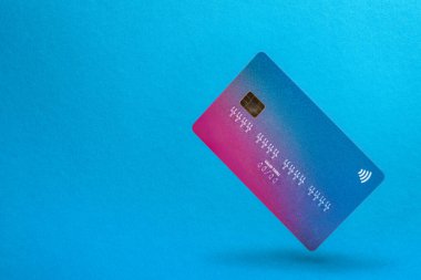 Mavi arka planda gölgesi olan boş bir kredi kartı havada süzülüyor. Metin eklenecek yeri olan kredi kartı. Ödeme ve banka transferleri kavramı.