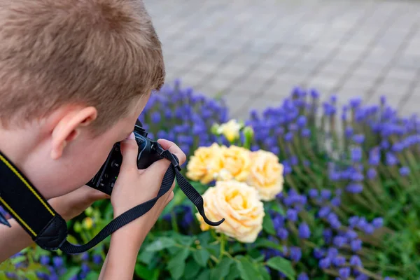 Un niño fotografía flores con una cámara SLR en el jardín de verano. — Foto de Stock