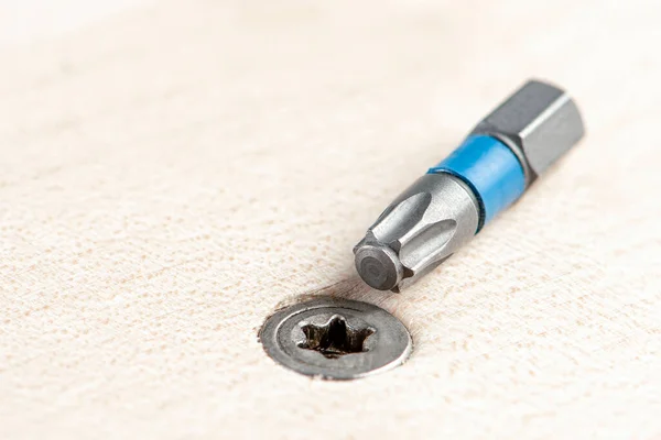 Screw the screw into the board. Furniture production, a screwdriver twists a self-tapping screw into a board. Several silver screws lie on the desktop — Stock Photo, Image