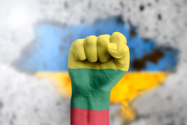 Литва помогает Украине и солидарна с ней. Концепция гуманитарной помощи Украине. Кулак окрашен в цвета литовского флага на фоне украинского флага. — стоковое фото