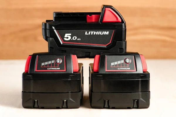Lithium battery for cordless drill. Screwdriver battery. Four batteries with a charge indicator lie on a wooden background.