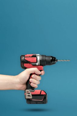Elimde kablosuz tornavida var. Bir erkeğin elindeki kablosuz alet. Mavi arka planda tamir ve inşaat kavramı