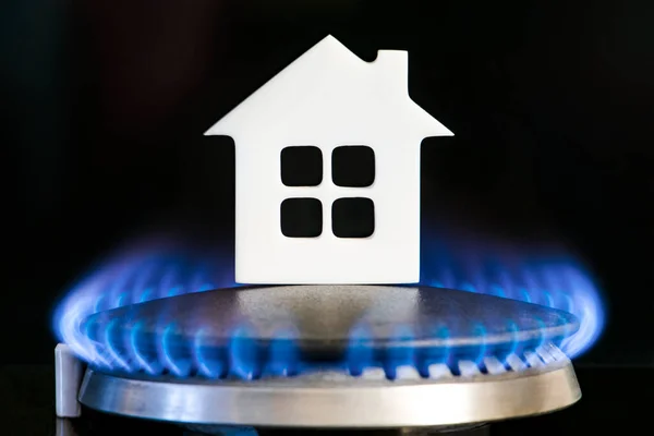 Heating season. The beginning of the heating season on natural gas. Concept, model of a house stands near the flame of a gas boiler on a black background. Home heating cost