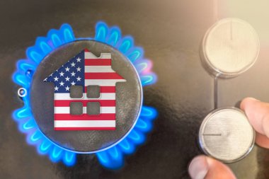Heating season or gas use in United States of America. Concept, model of a house stands near the flame of a gas boiler on a black background. The cost of using natural gas in USA