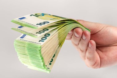 Stack of euro bills in hand. A large stack of 100 euro banknotes in a male hand on a uniform gray background. The concept of financial assistance, real estate purchase, loan or insurance payment