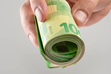 The hand holds a roll of 100 euro banknotes. Euro banknotes rolled up in a white mans hand on a gray background. The concept of financial assistance, real estate purchase, loan or insurance payment