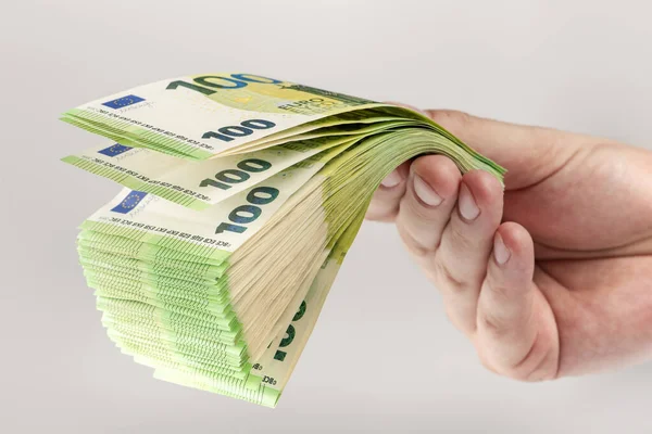 Stack of euro bills in hand. A large stack of 100 euro banknotes in a male hand on a uniform gray background. The concept of financial assistance, real estate purchase, loan or insurance payment