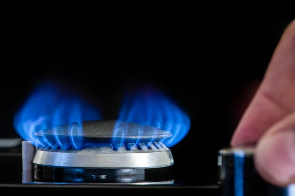 Gas stove on a black background. Fragment of a gas kitchen stove with a blue flame, close-up. Energy crisis concept, rise in price or price of gas