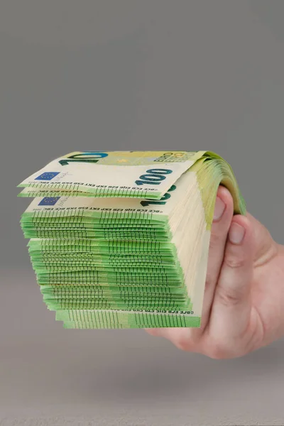 Large stack of euros in hand. Banknotes of 100 euros in a male hand on a uniform background. A man holds out his hand with a stack of banknotes as a concept of a loan, insurance payment or mortgage