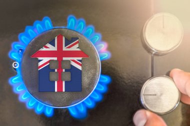Heating season or gas use in United Kingdom. Concept, model of a house stands near the flame of a gas boiler on a black background. The cost of using natural gas in United Kingdom