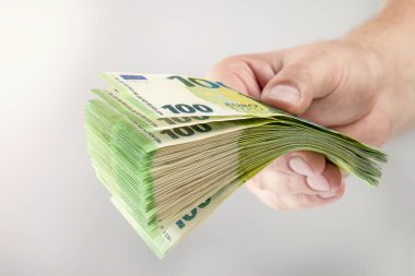 Large stack of euros in hand. Banknotes of 100 euros in a male hand on a uniform background. A man holds out his hand with a stack of banknotes as a concept of a loan, insurance payment or mortgage